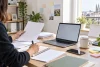 Une entrepreneuse organise des documents de création d’entreprise devant un ordinateur.